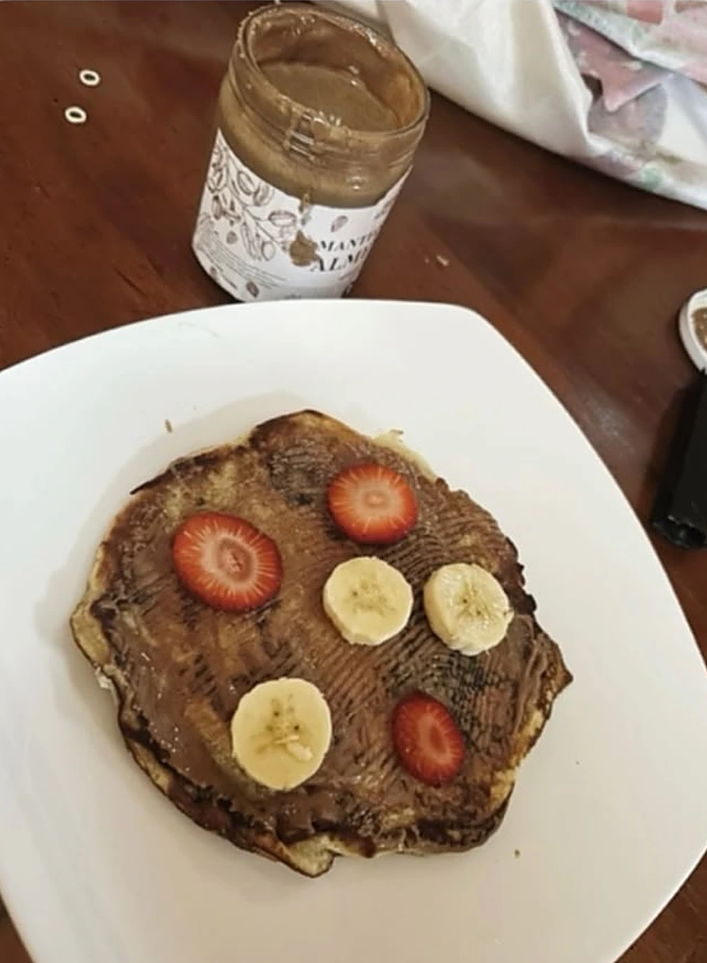 Panqueque con mantequilla de almendra, fresas y banano, junto al frasco